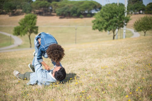 Father Lying Down on Grass and Playing with Son at Park