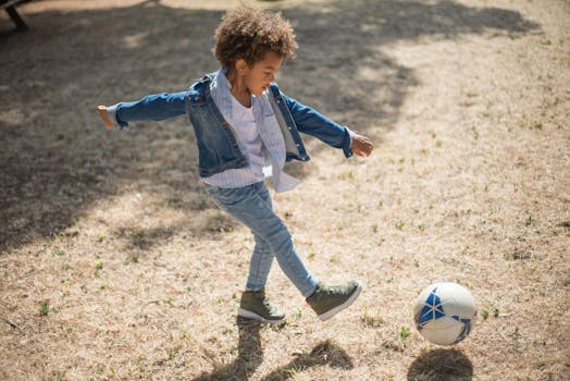 A young boy with curly hair kicks a soccer ball outdoors on a sunny day in Portugal.