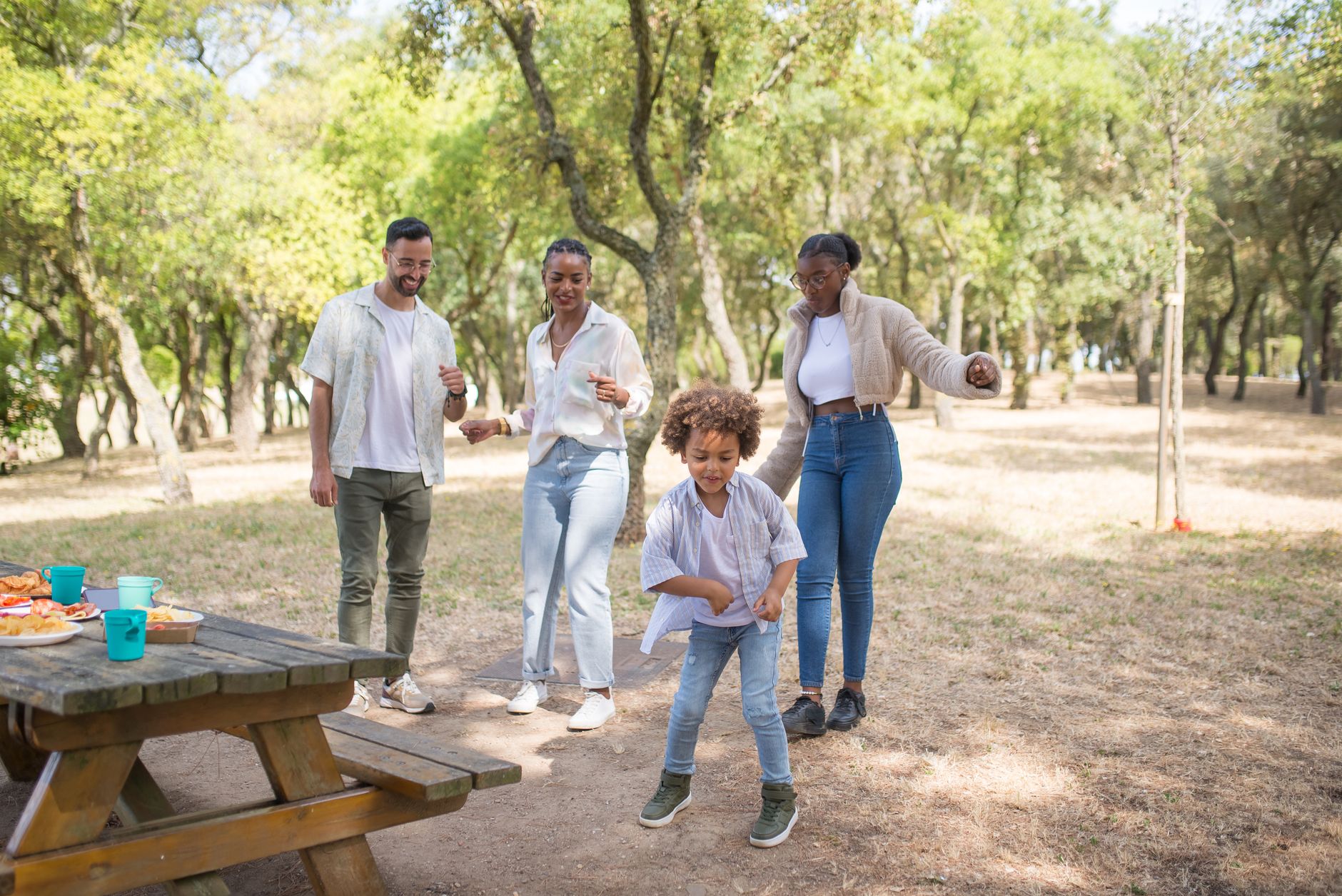 A family enjoys dancing together during a picnic in a sunny park.