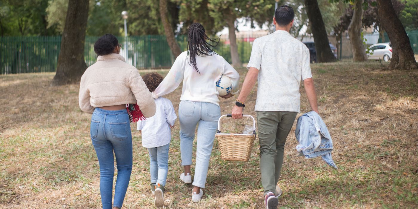 Family walking together carrying picnic basket in a sunny park.