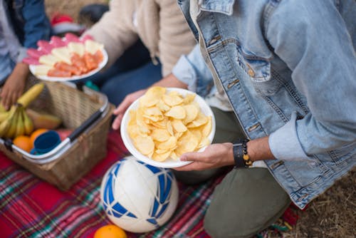 Person in Blue Denim Jacket Holding White Round Plate With Potato Chips