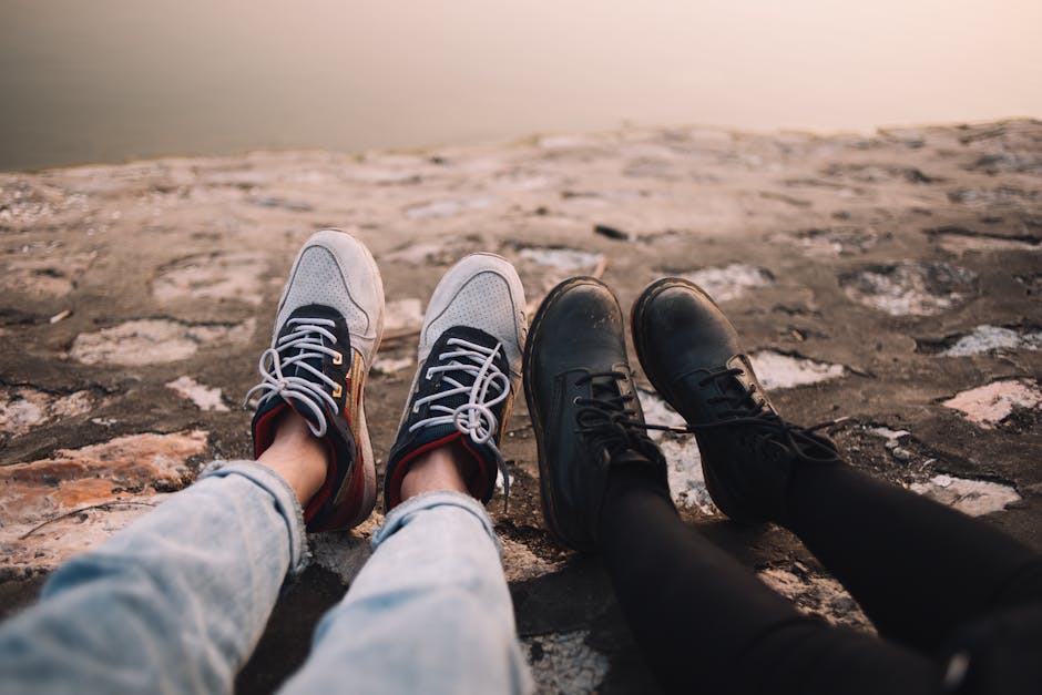 Two pairs of shoes on cobblestone by a tranquil lake, enjoying sunset vibes.
