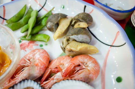 Appetizing seafood platter featuring shrimps, snails, and edamame beans on a decorative plate.