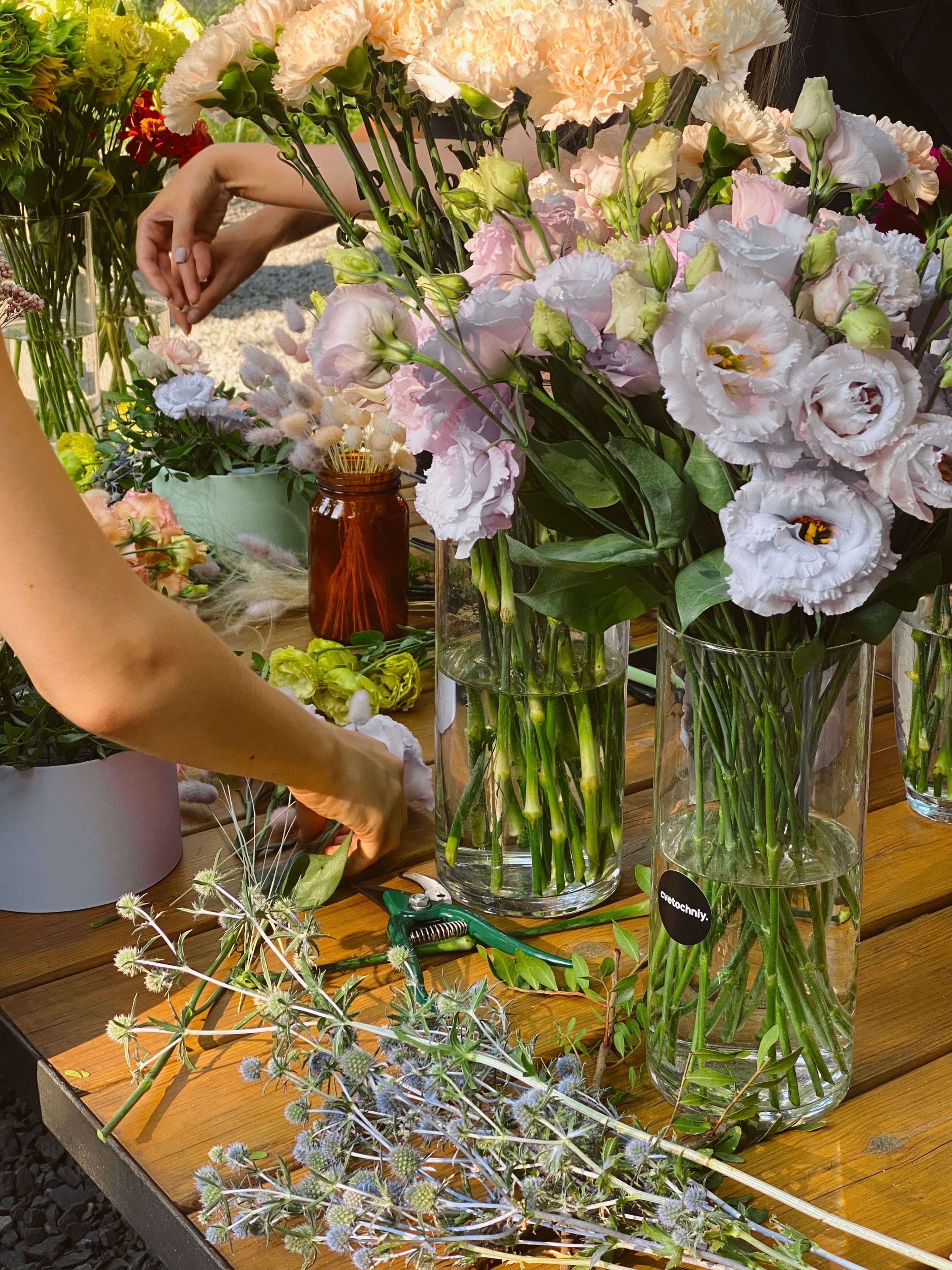 A bright collection of fresh flowers in glass vases on a wooden table with hands arranging them.