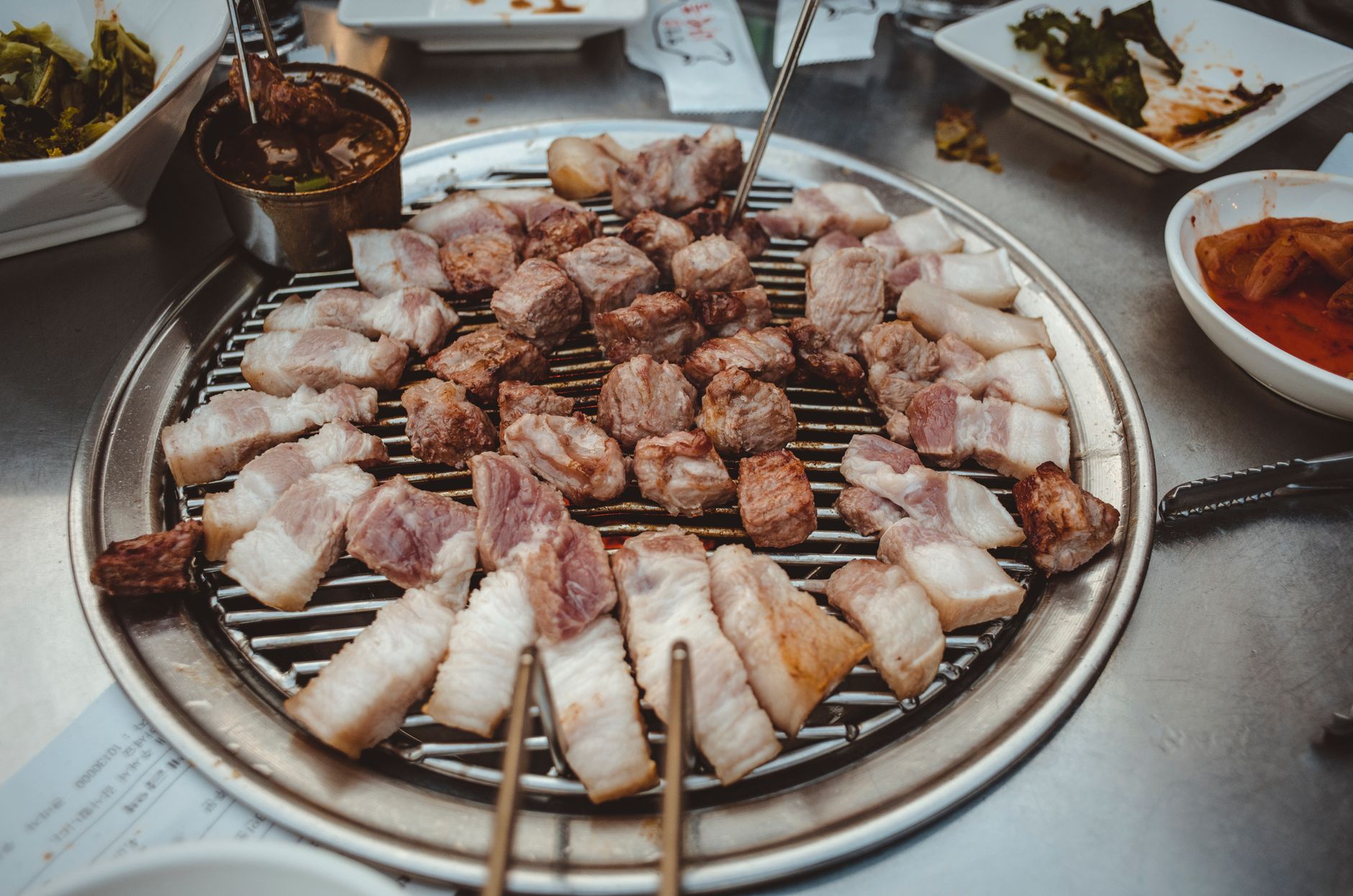 Sizzling slices of meat cooking on a traditional Korean barbecue grill with delicious side dishes.