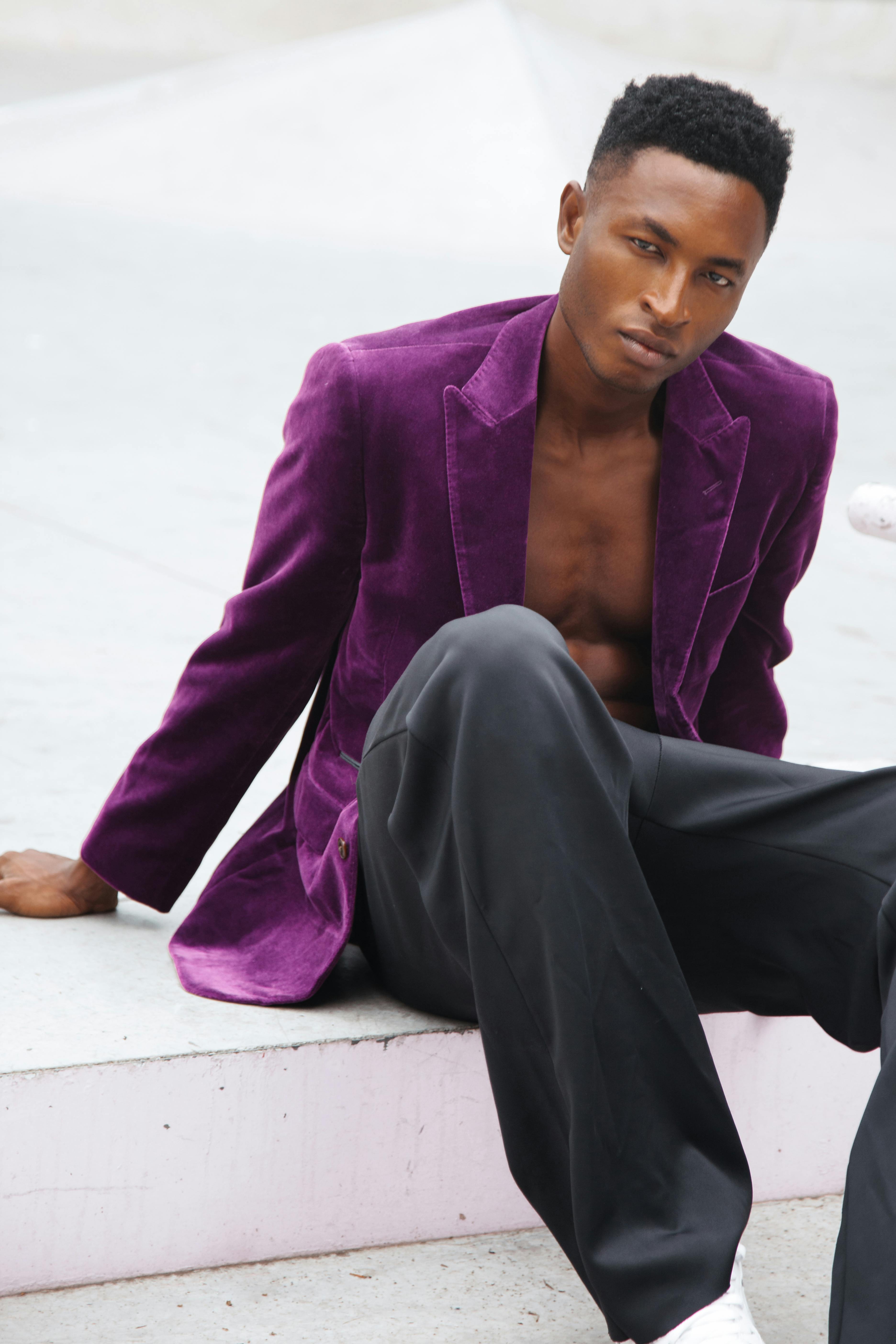 Fashionable adult male model in vibrant purple velvet blazer posing on an urban outdoor setting.