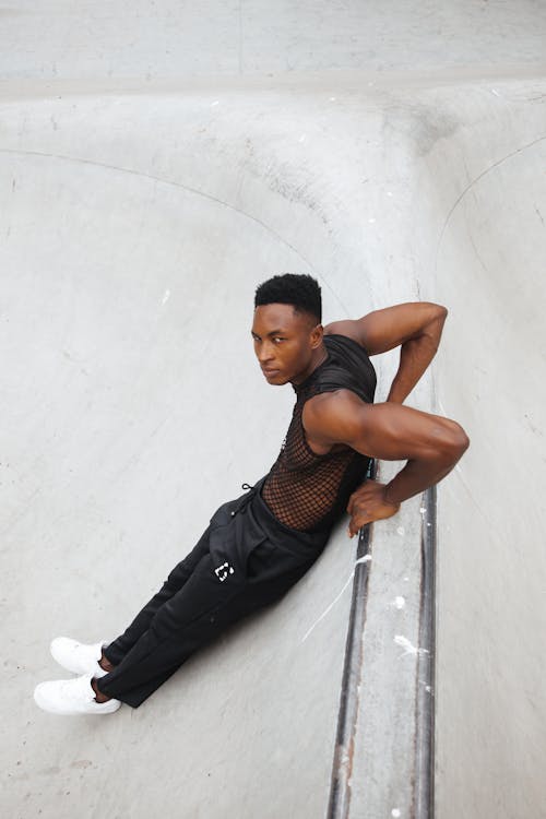 A High Angle Shot of a Man in Black Tank Top and Pants Leaning on the Wall