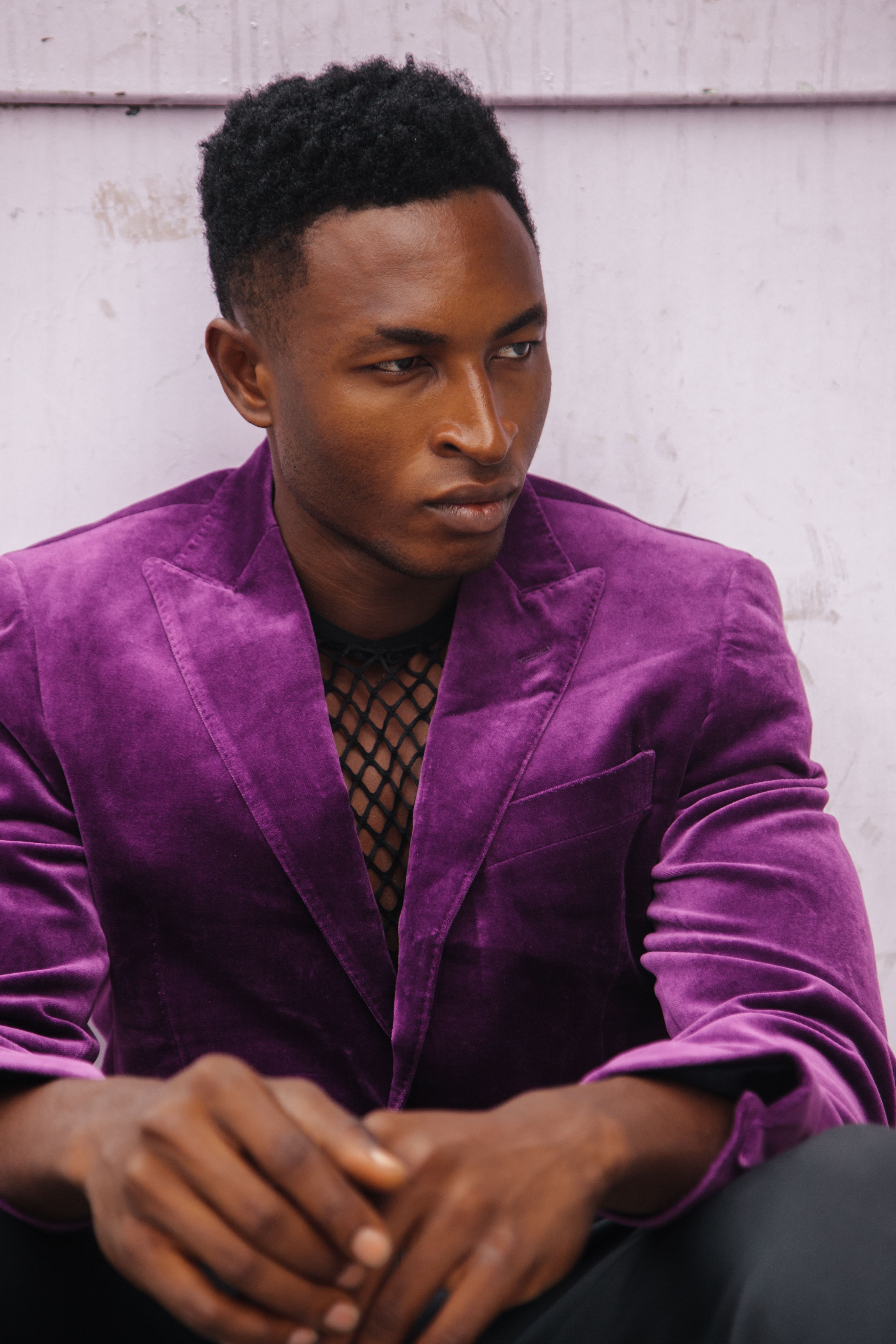 Stylish man in a vibrant purple velvet blazer, seated and pensive.