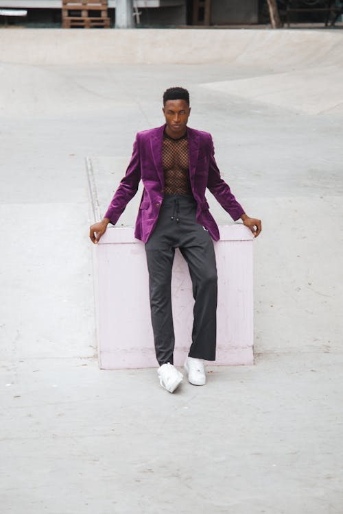 Man in Purple Blazer and Gray Pants Standing on a White Concrete Wall