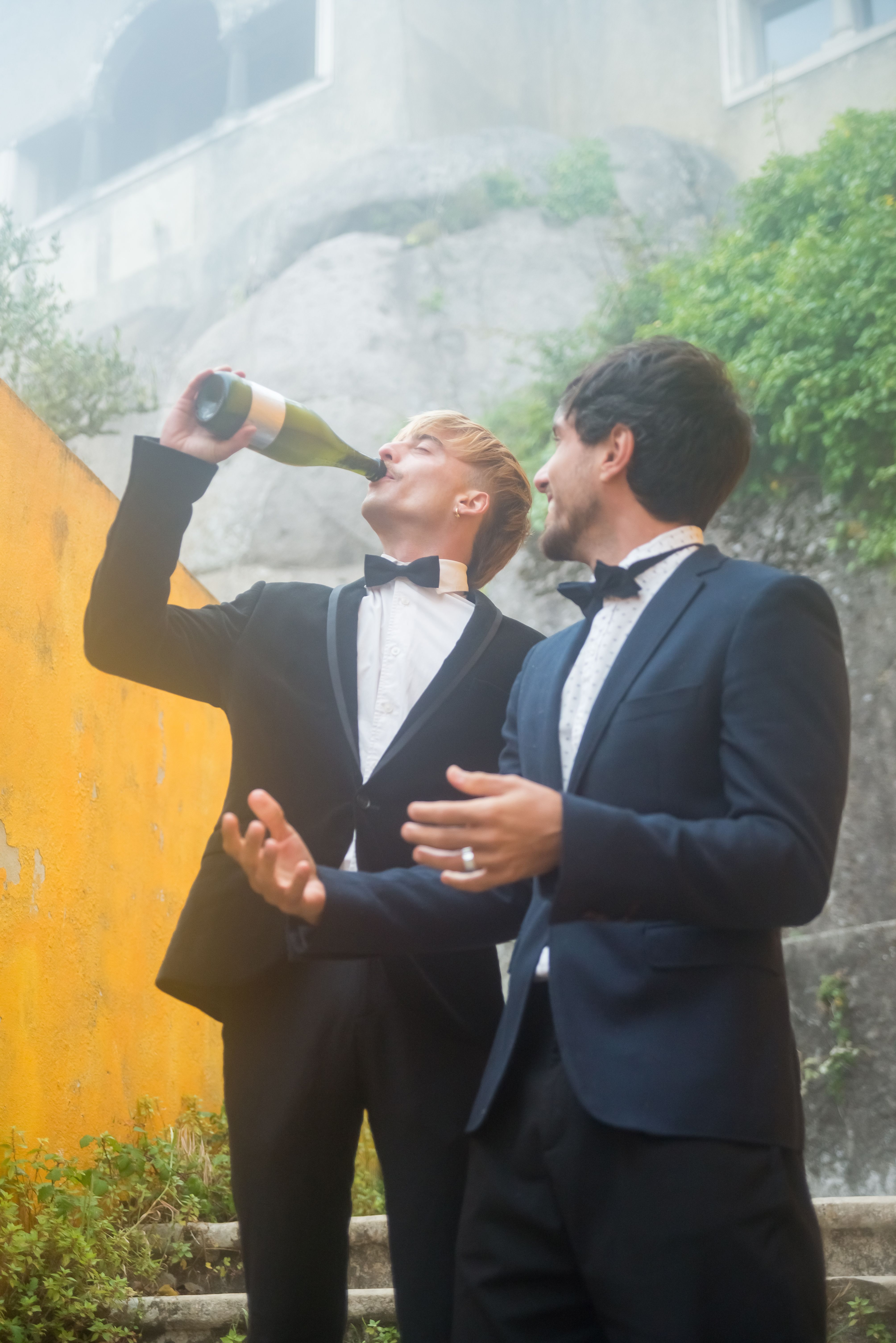 Friends in black suits celebrating outdoors with champagne in Portugal.