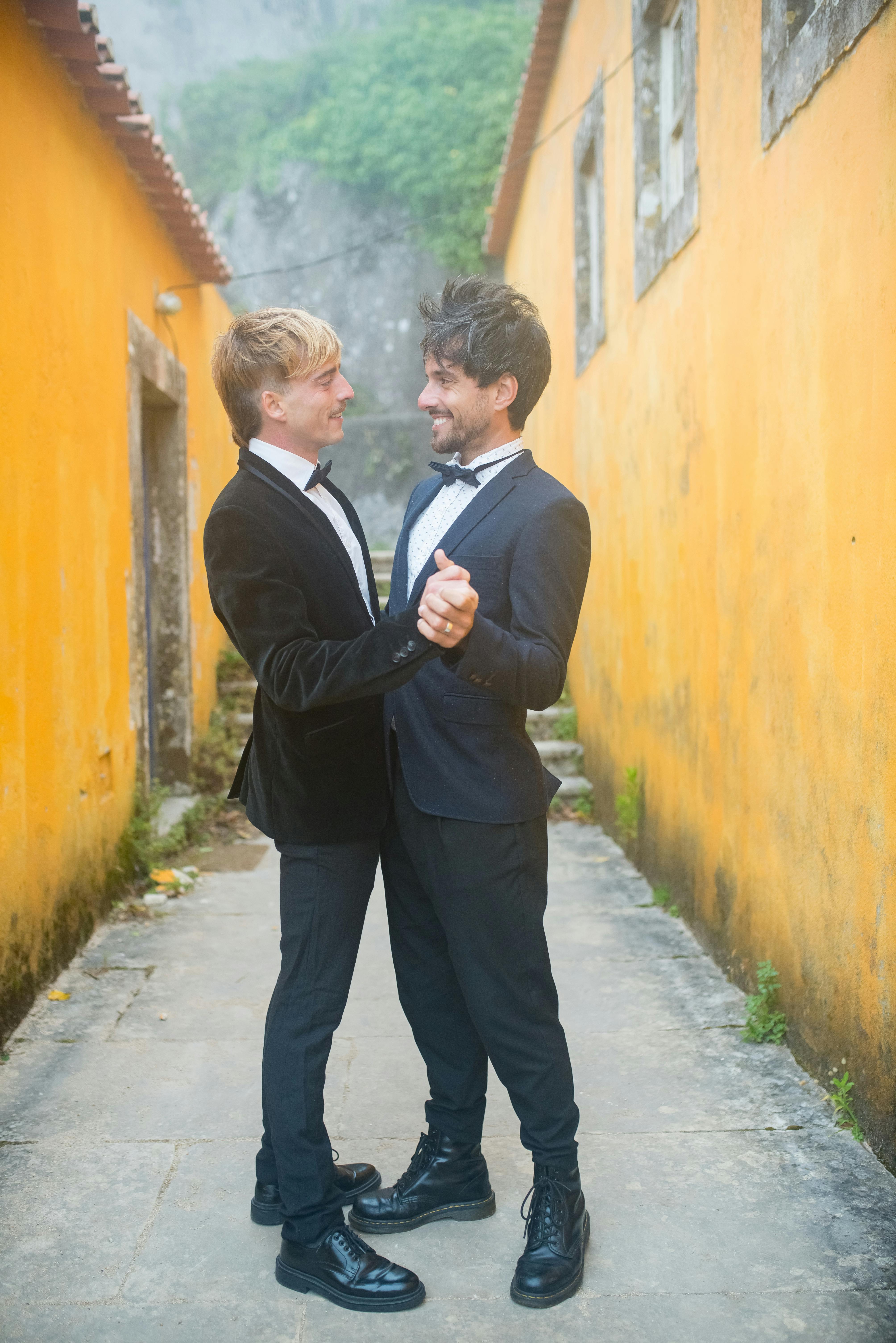 two men in black suit holding hands and smiling