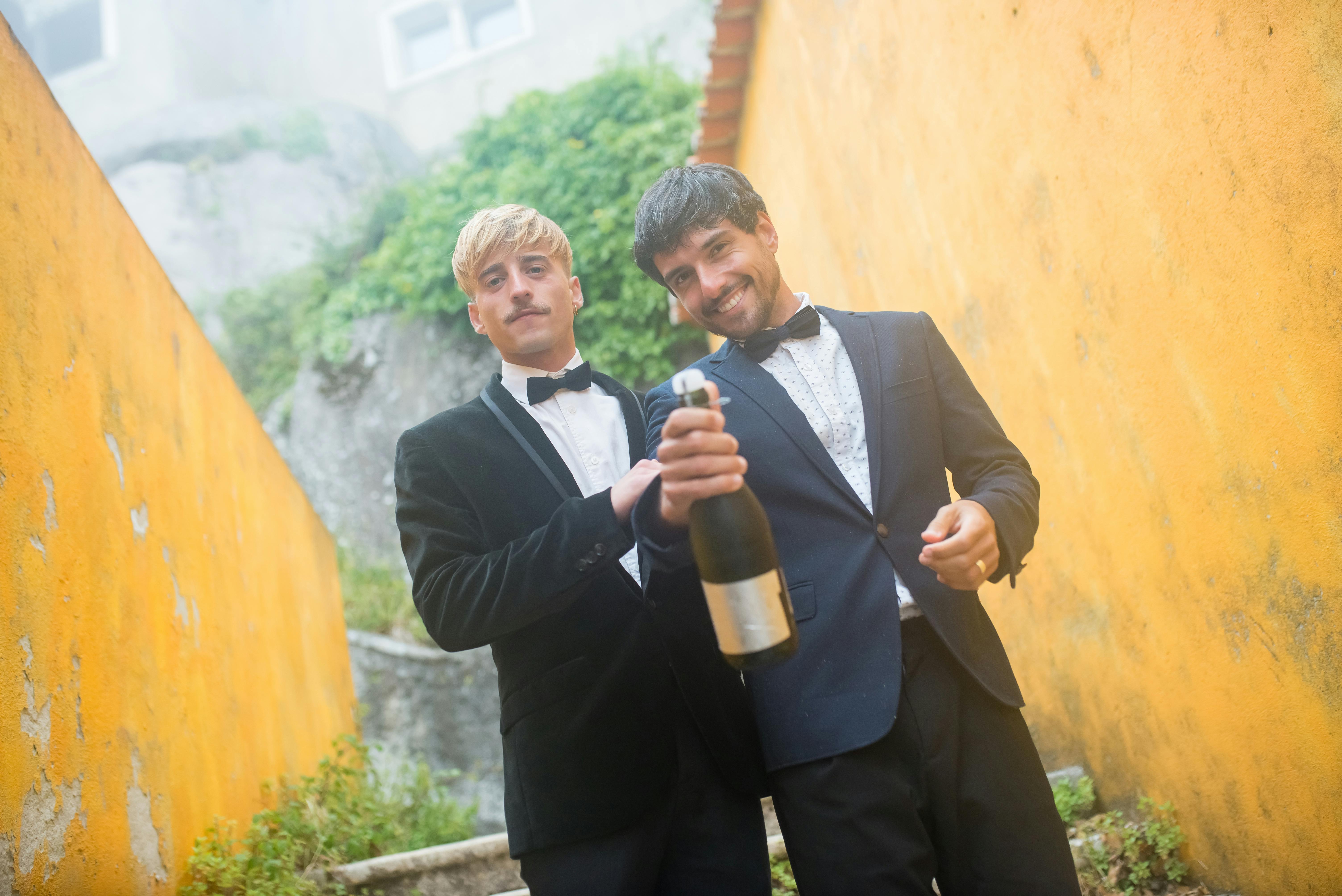 Two men celebrating with champagne outdoors in Portugal, wearing tuxedos and smiling.