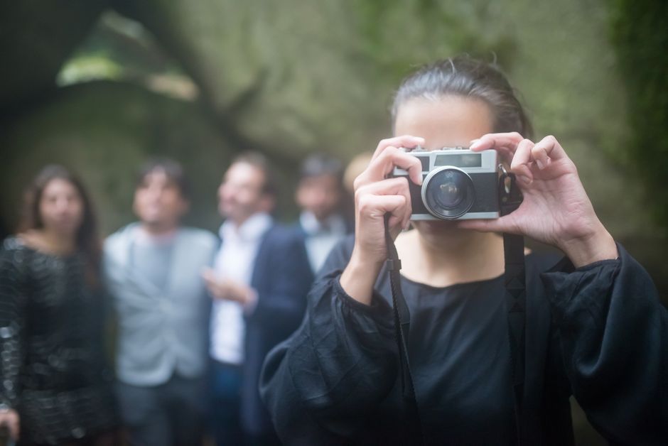 Woman taking photo of guests in outdoor setting, capturing memorable moments.