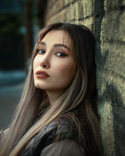 Free A stylish portrait of a woman standing against a city wall, characterized by a moody atmosphere. Stock Photo
