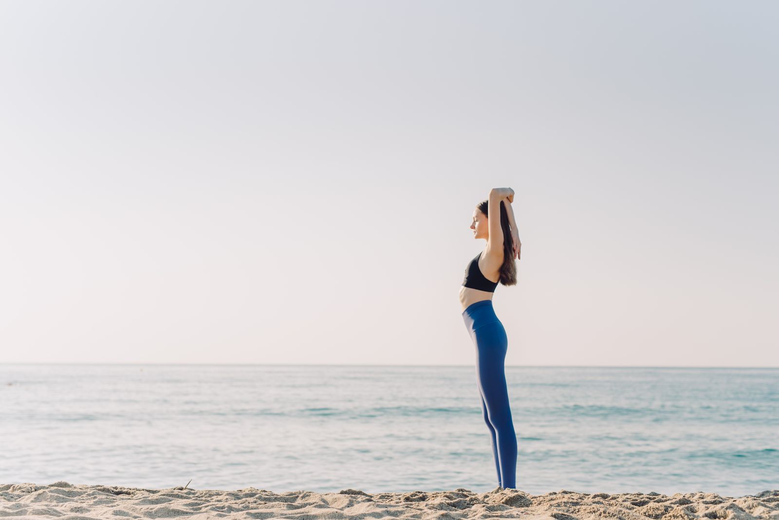 Woman practicing a yoga pose on a beach under clear blue sky