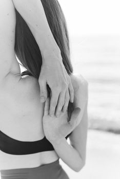 A woman stretching her arms while facing the sea in a black and white photo.
