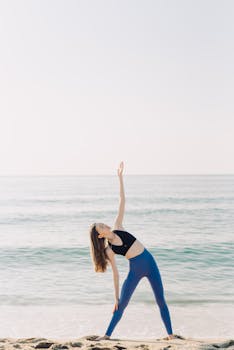 A woman performs yoga poses on a serene beach during sunrise, promoting wellness and flexibility.