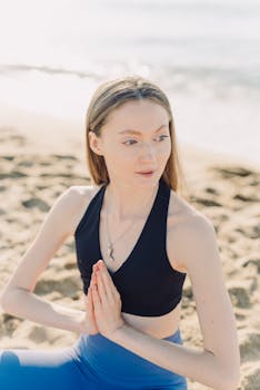 A woman practicing yoga on a sandy beach during sunrise, embodying peace and balance.