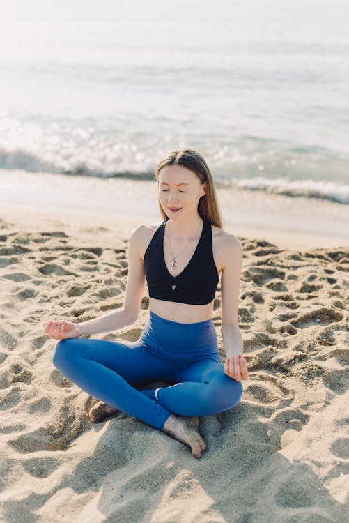 Free Woman in Black Tank Top and Blue Denim Jeans Sitting on Beach Sand Stock Photo