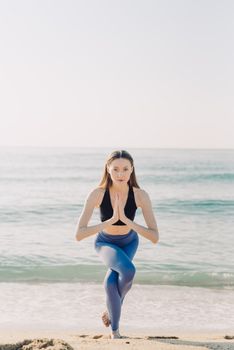 A woman in sportswear performing yoga on a sunny beach, symbolizing health and wellness.