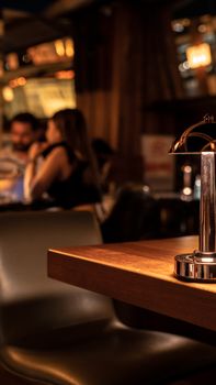 Warm and inviting restaurant ambiance featuring a lamp on a wooden table with blurred patrons in the background.