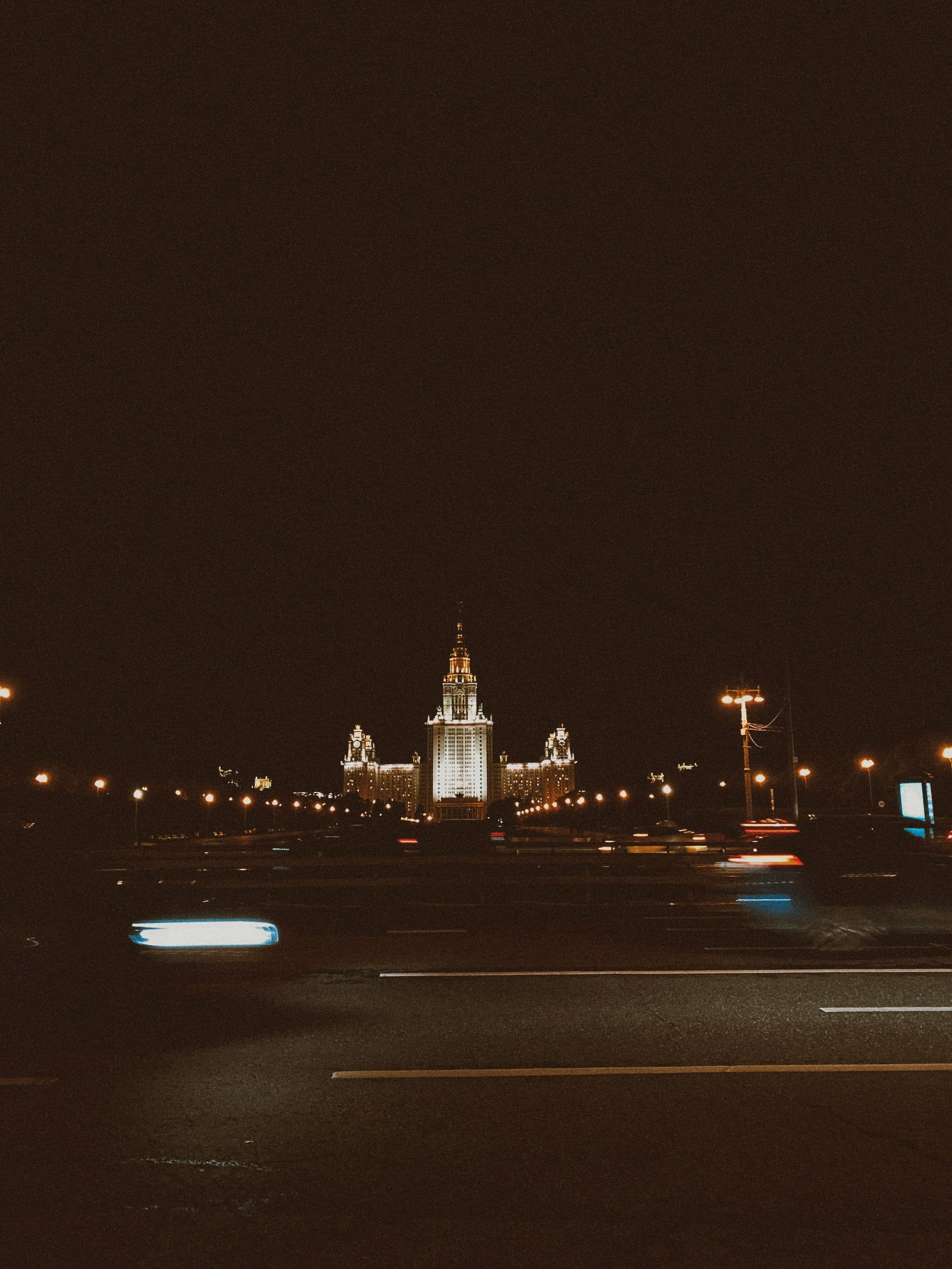 A majestic city tower beautifully lit against the night sky, captured with blurred motion car trails.