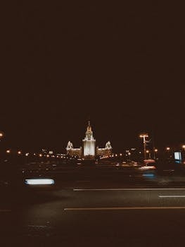 A majestic city tower beautifully lit against the night sky, captured with blurred motion car trails.
