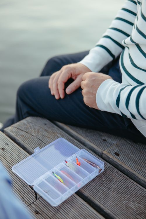 Free A person sitting on a wooden dock with fishing equipment in a plastic case. Stock Photo