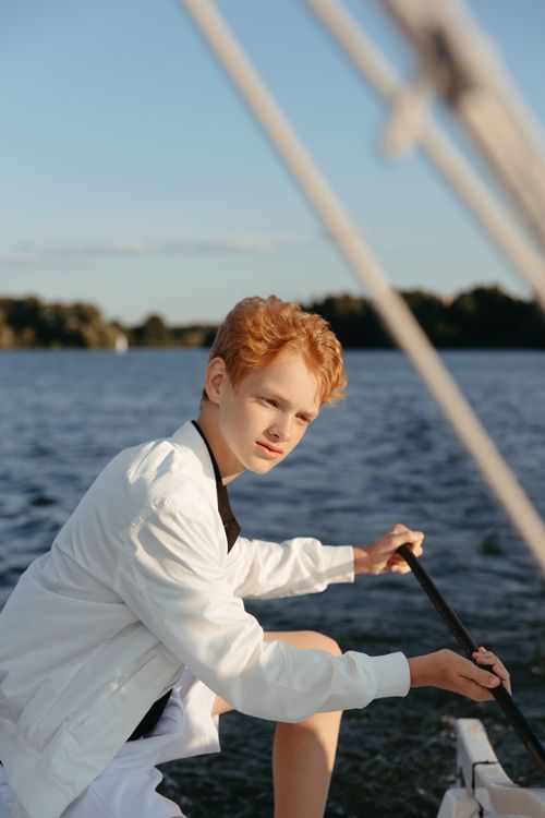 Free A young boy with red hair enjoys sailing on a serene lake on a sunny summer day. Stock Photo