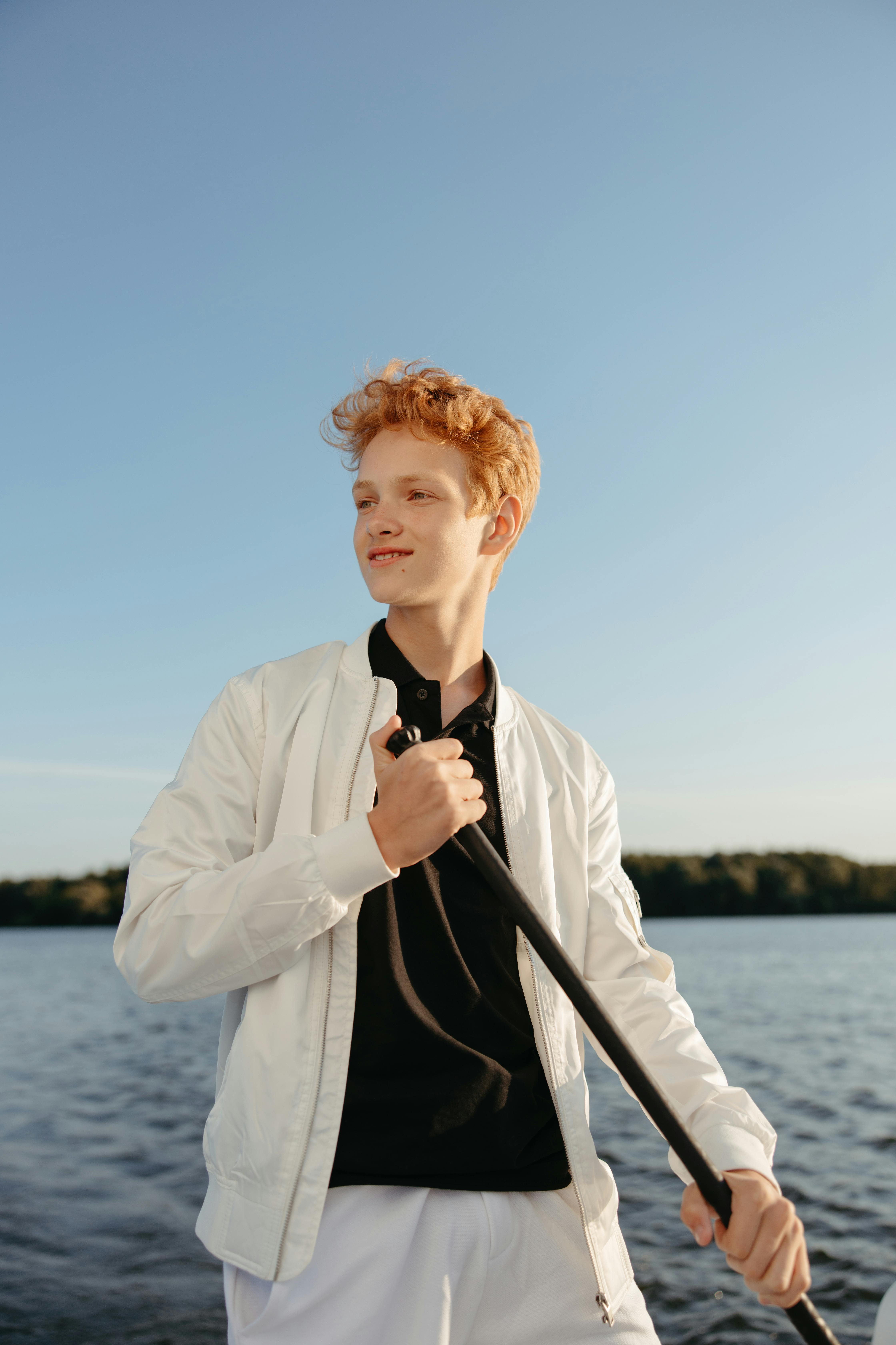 Young man smiling while standing on a boat holding a paddle under a clear sky.