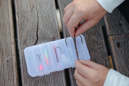 Hands organizing fishing hooks in a plastic case on a wooden surface. Perfect for fishing enthusiasts.