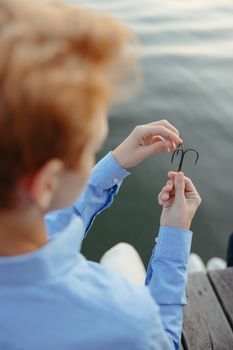 Person in blue shirt holding fishing hooks over a dock by the water.