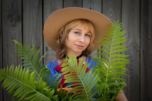 Free A young woman poses outdoors, wearing a hat and holding ferns, creating a natural portrait. Stock Photo