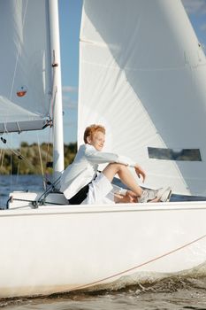 Teen boy relaxing on a sailboat during a sunny day, enjoying the peaceful water and breeze.