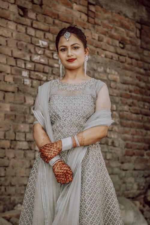 Woman in White Lace Dress Standing Beside Brown Brick Wall