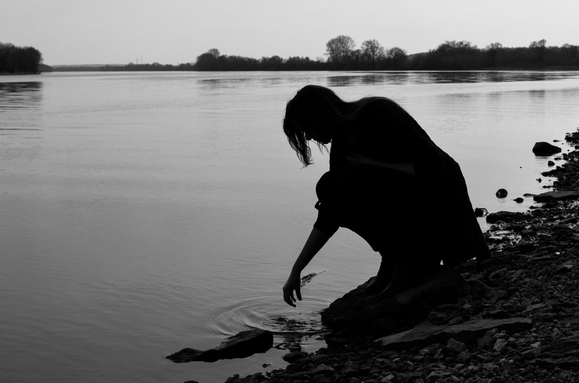 Silhouette of person touching water by a calm lake, Kolomna, Russia. Serene and introspective scene.
