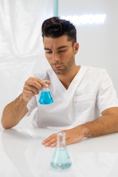 Young scientist in white coat examining blue liquid in a lab flask, focused and professional setting.