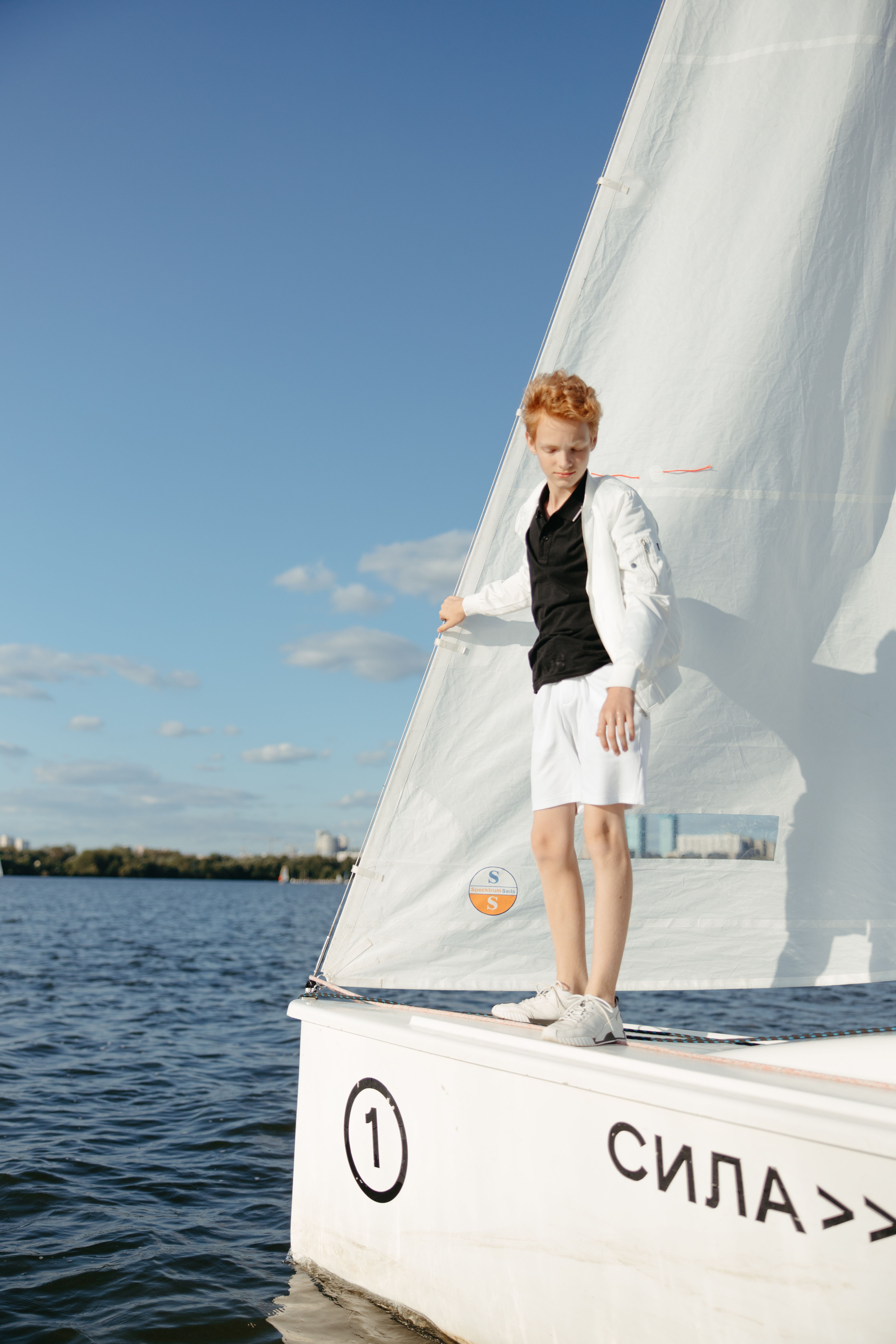 A teenager sailing on a small boat in the ocean, enjoying a bright sunny day.