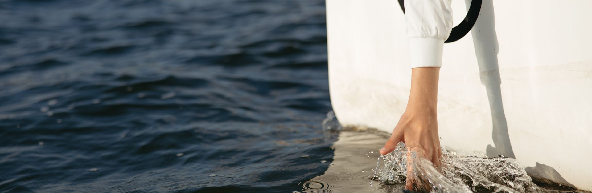 A hand gracefully touches ocean water from a boat, creating a ripple effect in the sunlight.