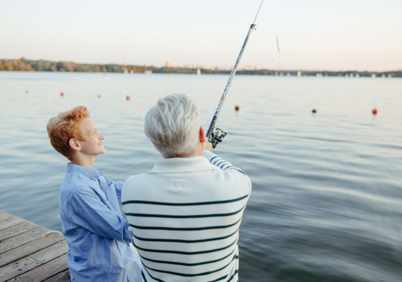 A grandfather and grandson fishing side by side from a dock