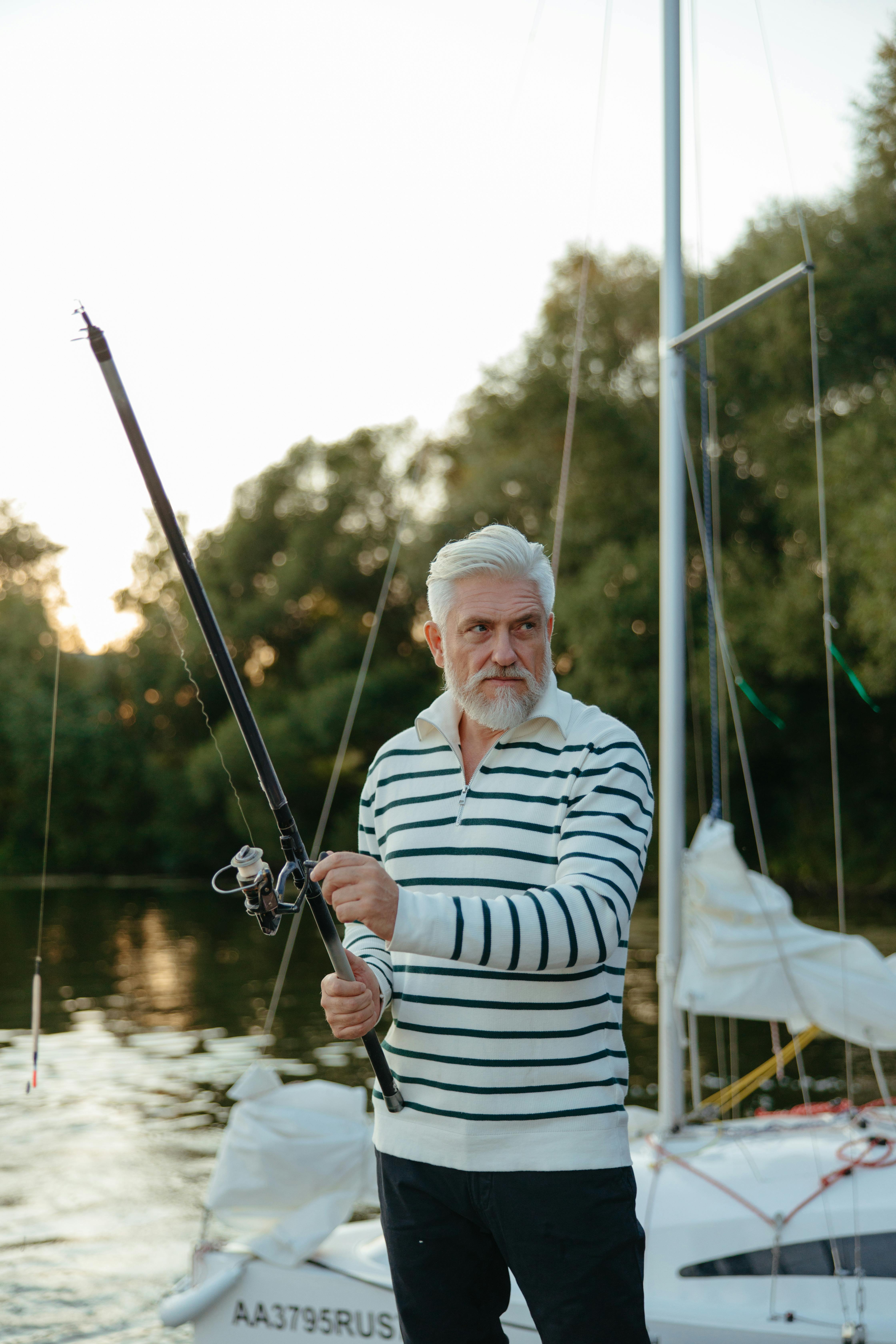 Elderly man enjoys fishing on a sailboat during a serene sunset by the water.