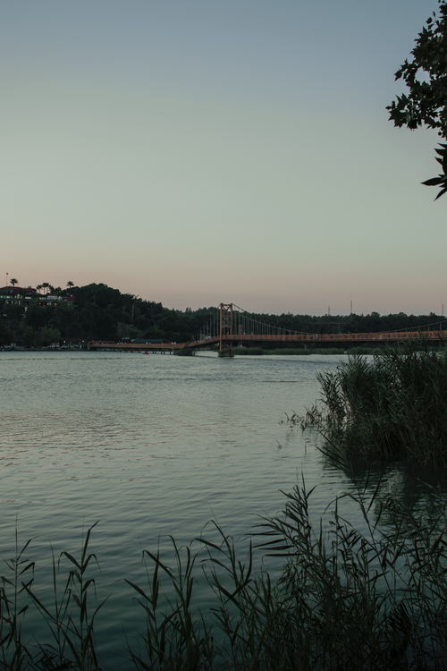 Free Peaceful scene featuring a bridge over a calm lake surrounded by greenery at sunset. Stock Photo