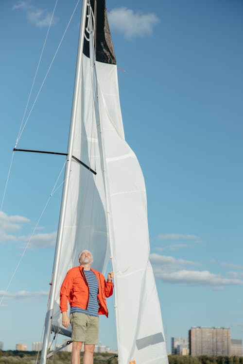 Man in Orange Jacket Standing on White Sailboat