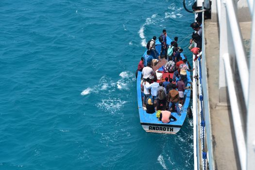 A crowded boat docking next to a ship in the vibrant blue waters of India.