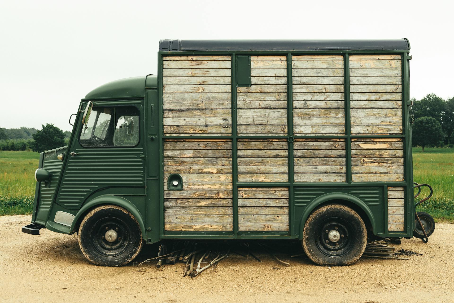 A vintage green food truck with a wooden exterior parked on a rural dirt road in a countryside setting.