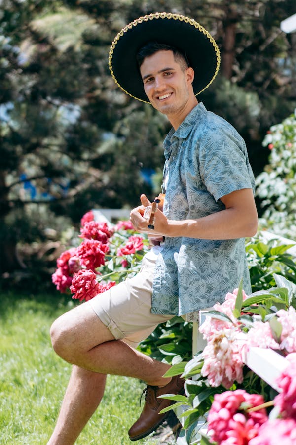 A Young Man Wearing Sombrero Sitting on Wooden Fence with Flowers
