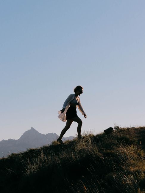 Silhouetted woman walking uphill against a clear sky with distant mountains.