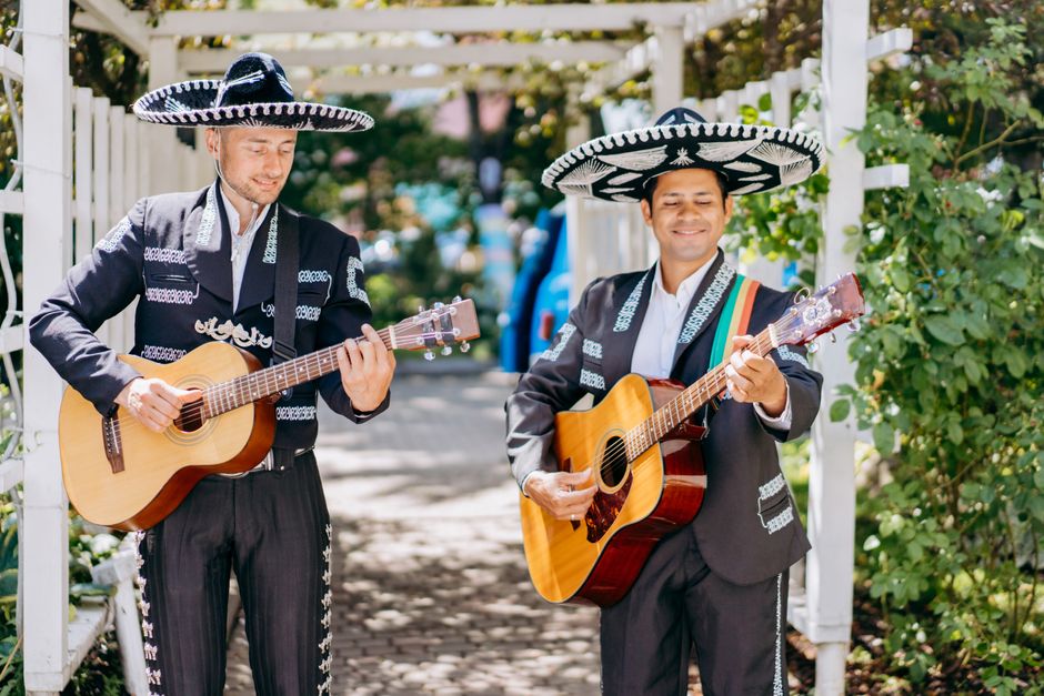 Two mariachi musicians in traditional attire performing with guitars outdoors, creating a lively and cultural scene.