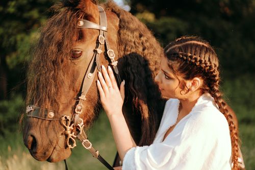 Free A woman with braided hair gently touches her black horse outdoors, bathed in warm sunlight. Stock Photo