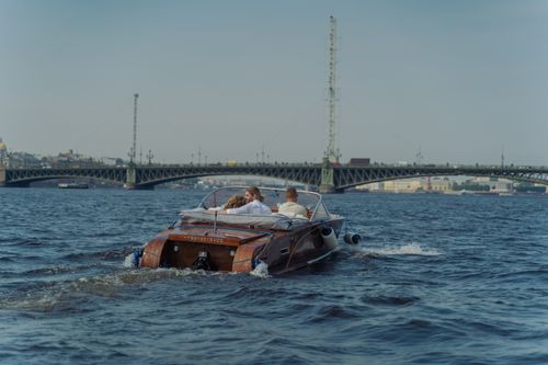 Free Couple enjoying a speedboat ride on a scenic river with a bridge view. Stock Photo